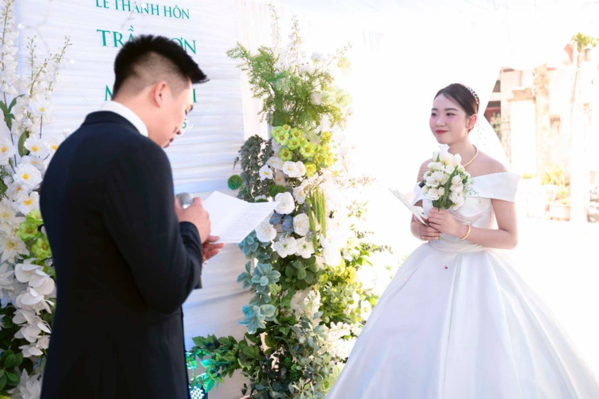 Chú rể xúc động đọc lời thề nguyện trước cô dâu trong lễ cưới, phía sau là sân khấu trang trí hoa tươi tinh tế. (Ảnh: Sưu tầm)