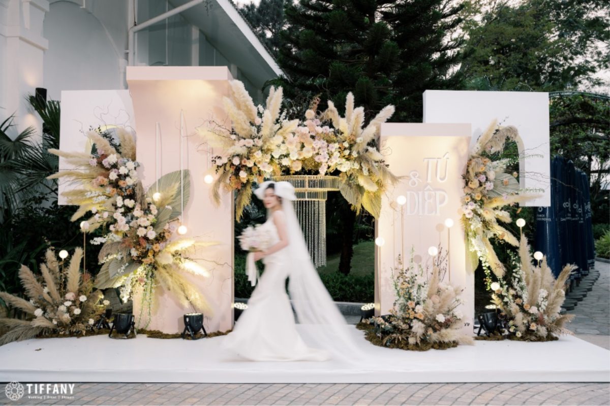 Một cổng hoa hoang dã được kết từ cỏ lau, hoa nhí và vài nhành lá khô – như mang cả sắc trời đồng nội vào không gian cưới. (Ảnh: TIFF.vn)
