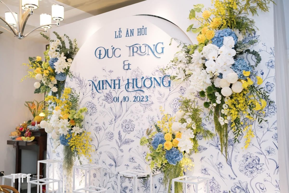 Backdrop lễ ăn hỏi màu trắng trang nhã, kết hợp hoa tươi tone vàng và xanh, điểm xuyết hoa trắng tạo không gian thanh lịch và tươi sáng. (Ảnh: Sưu tầm)