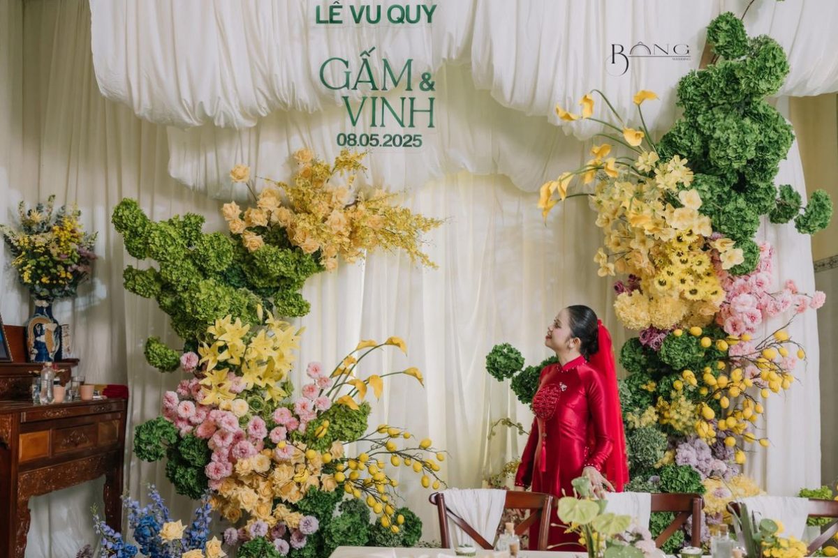 Cô dâu rạng rỡ trong áo dài đỏ, hòa cùng hoa màu vàng – tím và lá xanh, tạo nên khung cảnh cưới vừa nổi bật vừa đầy lãng mạn. (Ảnh: TIFF.vn)