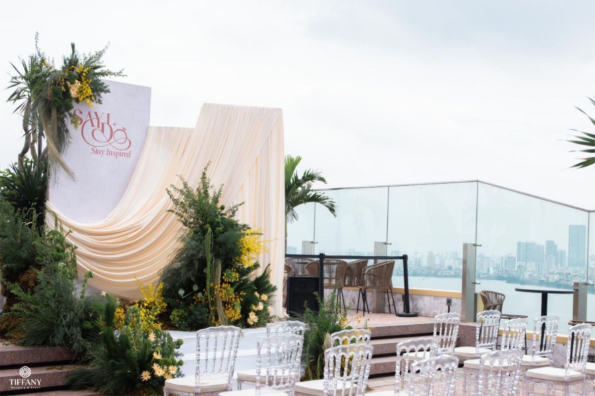 Không gian lễ vows ngoài trời Lotte L7 Westlake với hoa vàng, lá xanh, ghế trong suốt và view Hồ Tây. (Ảnh: TIFF.vn) 