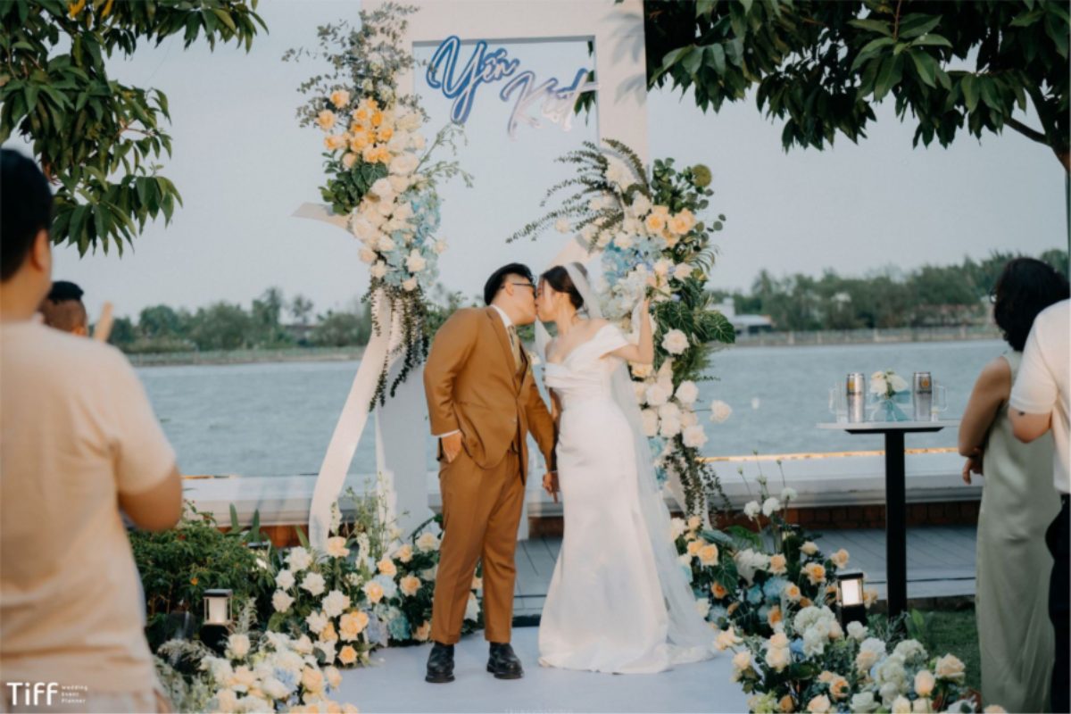 Cặp đôi trao nụ hôn dưới vòm hoa bên sông, phía sau là bến thuyền và cây xanh. (Ảnh: TIFF.vn)